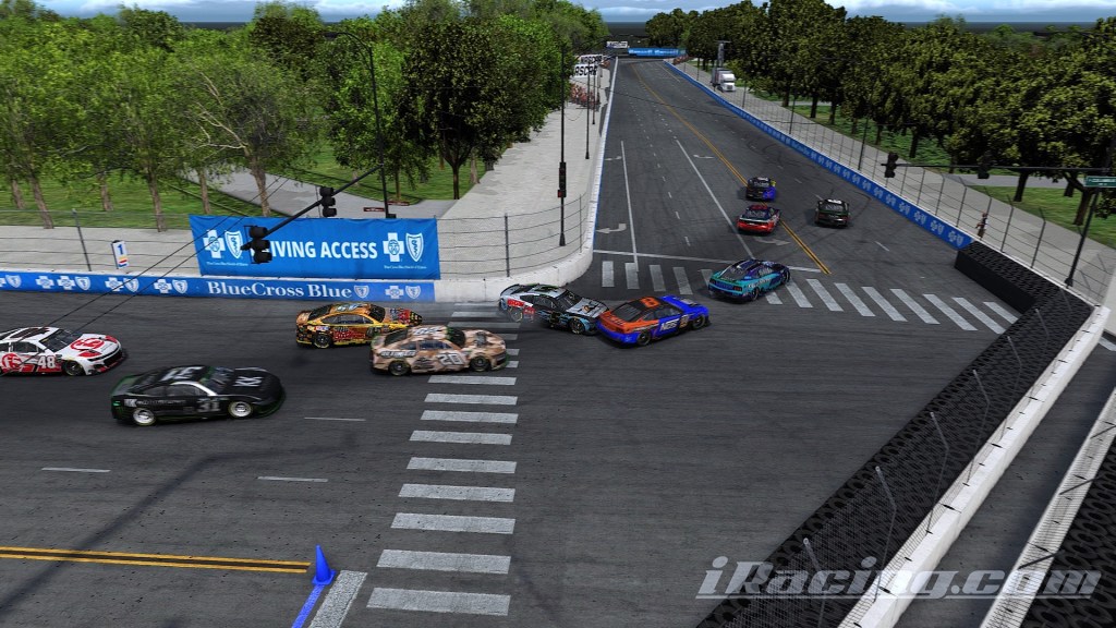 A chaotic racing scene featuring multiple cars in close proximity, with one vehicle making contact with a wall while others maneuver around a turn in an organized racing environment.