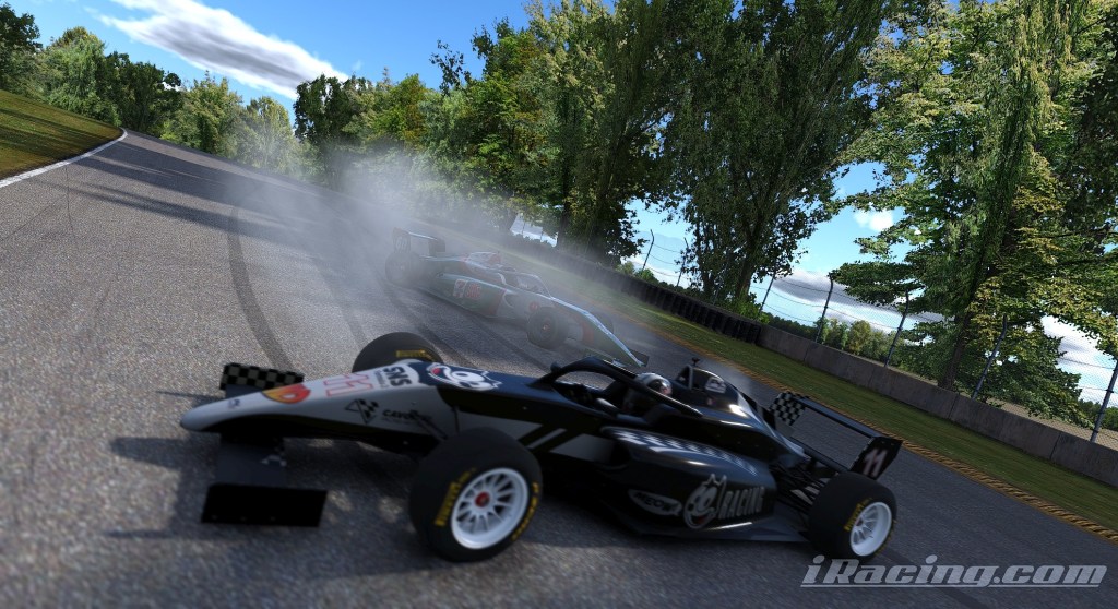 A close-up of two race cars on a track, with one car emitting smoke as it skids, surrounded by trees and a clear blue sky.