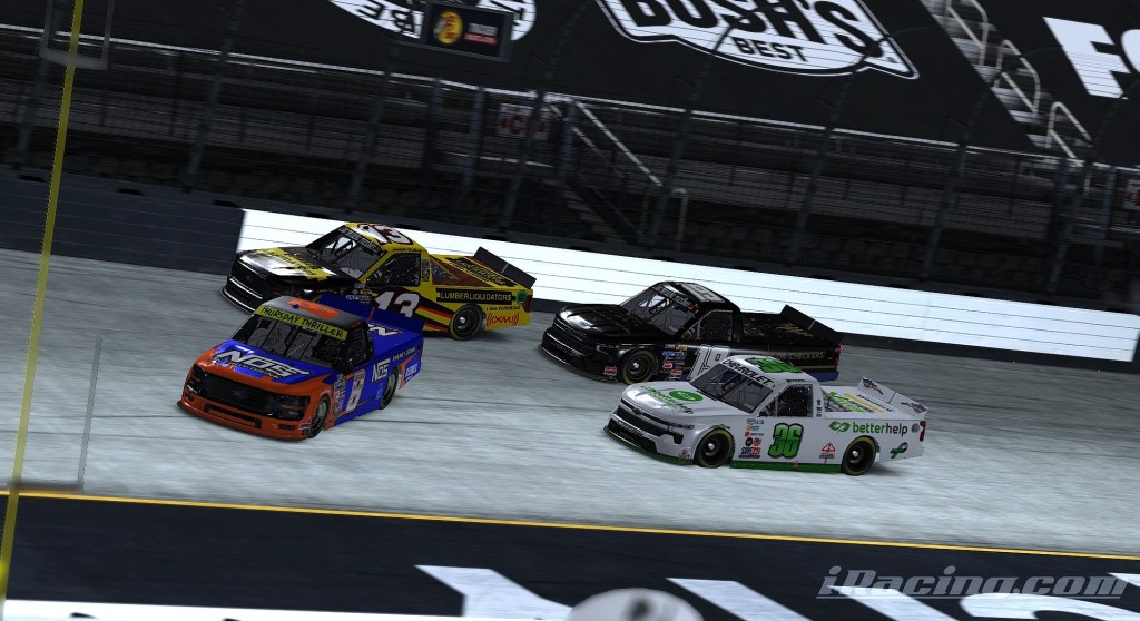 Four trucks racing closely together on the track, with one truck visibly leading while others attempt to overtake.