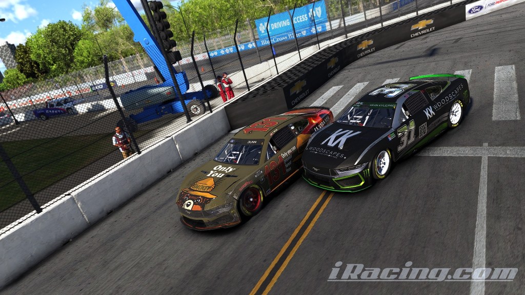 Two race cars competing closely on a racetrack, with the background showing a cheering crowd and a billboard.