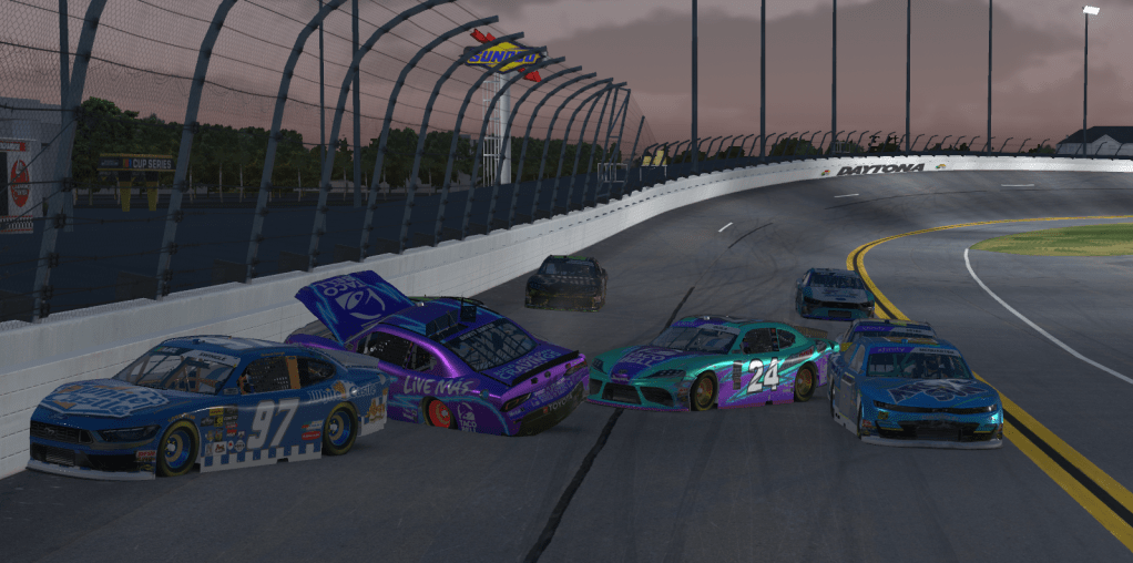 A multi-car collision at Daytona International Speedway during a race, with damaged cars and a twilight sky in the background.