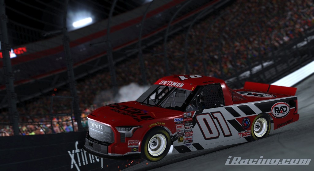A red and black racing truck number 01 on the track at Bristol Motor Speedway, surrounded by blurred motion and a cheering crowd in the stands.